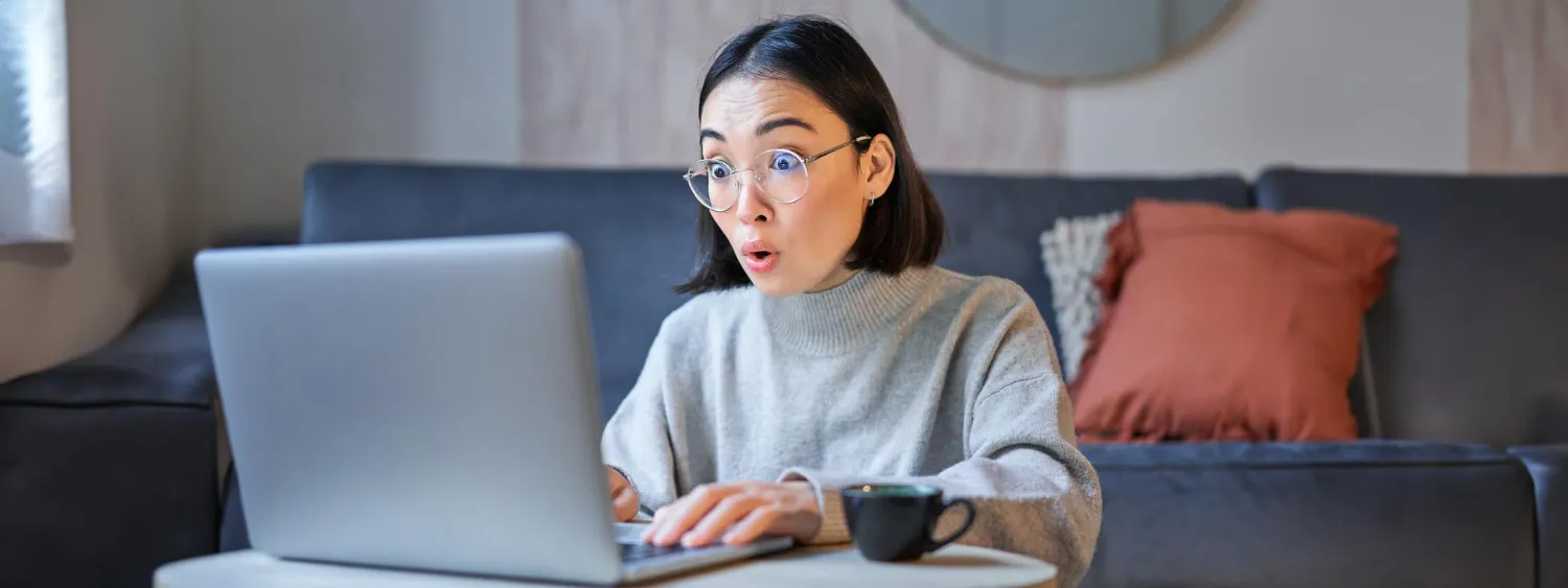 Portrait of asian woman in glasses sitting with laptop and looking surprised amazed by promotion on